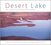 The cover image of Desert Lake, features an arial view of a dark blue lake with a river feeding into it in the middle of deep red desert. The cover image of Desert Lake, features an arial view of a dark blue lake with a river feeding into it in the middle of deep red desert.